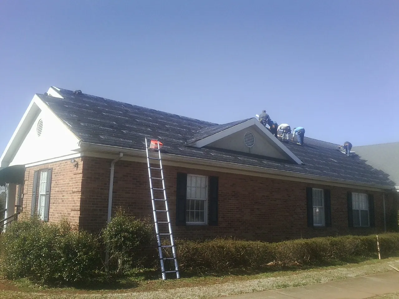 Crew tearing shingles off a brick ranch roof with a ladder set — Emergency Roof Repair work by our crew in Parkton