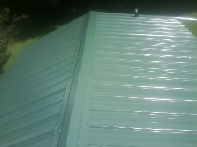 New green metal panels meeting at the ridge of a roof — Flat Roof Repair work by our crew in Parkton