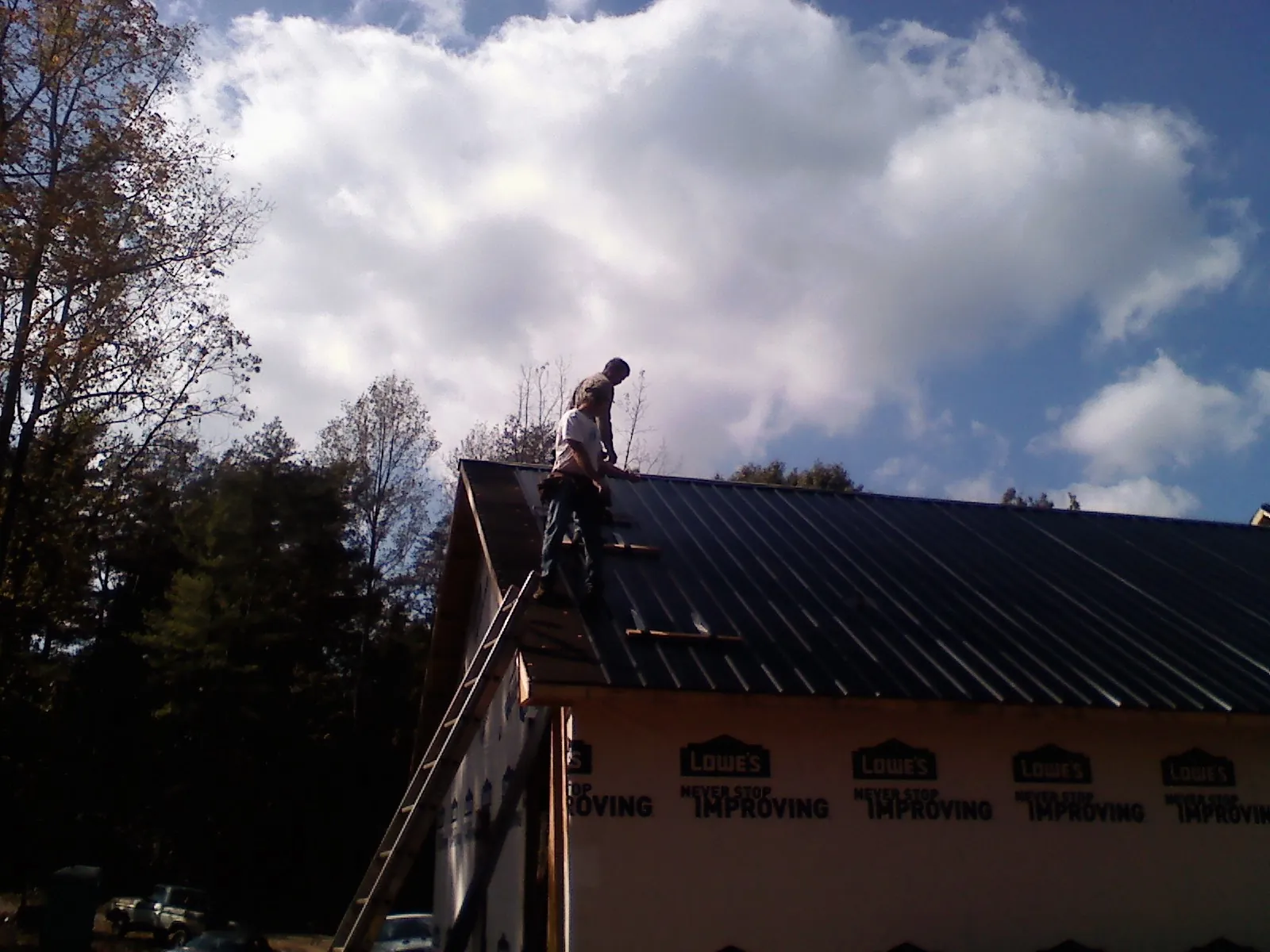 Roofer fastening dark metal panels high against a cloudy sky, from a Roof Inspection job in Parkton